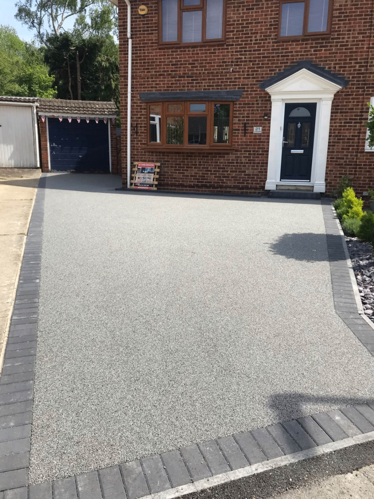 Light resin driveway with dark block border outside a brick house